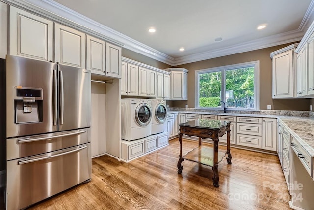 clothes washing area with washing machine and dryer, ornamental molding, and light wood-type flooring