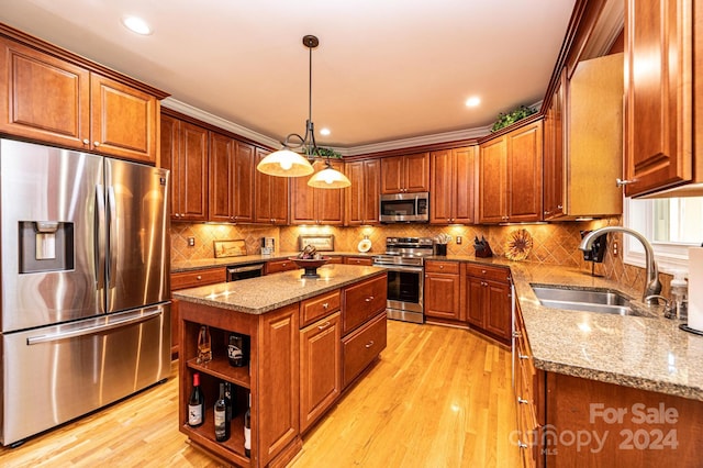 kitchen with a kitchen island, hanging light fixtures, sink, appliances with stainless steel finishes, and light hardwood / wood-style floors