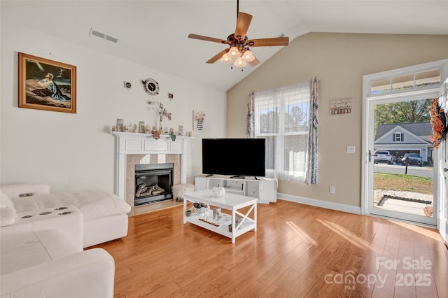 living room with a high end fireplace, light hardwood / wood-style flooring, ceiling fan, and lofted ceiling