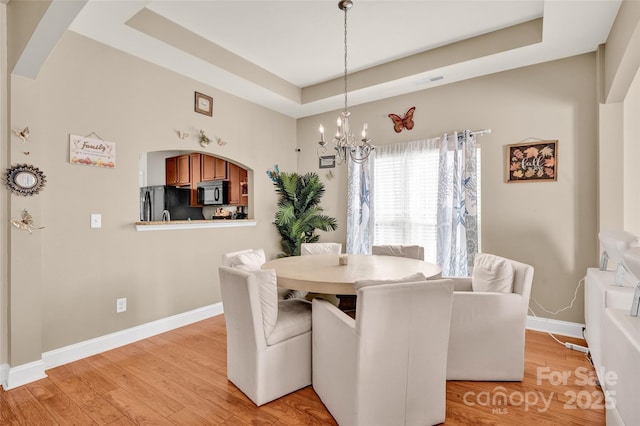 dining area featuring an inviting chandelier, light hardwood / wood-style flooring, and a tray ceiling