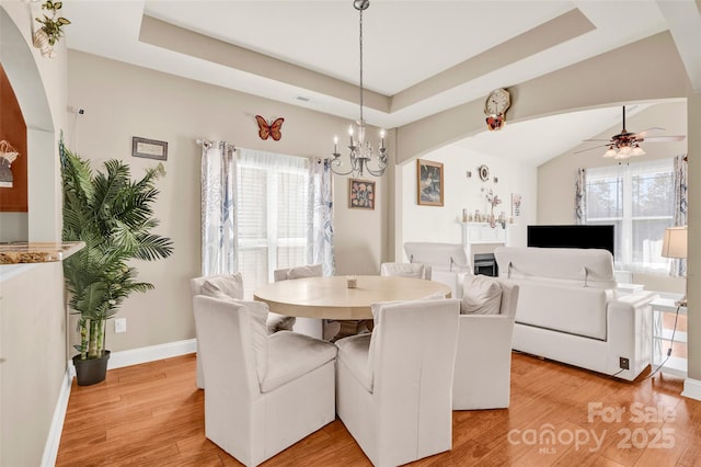 dining area with ceiling fan with notable chandelier, light wood-type flooring, and a tray ceiling