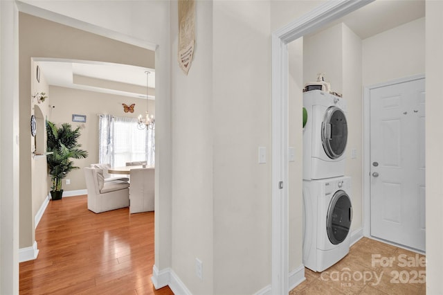 washroom featuring a chandelier, light wood-type flooring, and stacked washer and clothes dryer