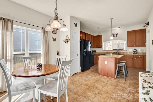 kitchen with a kitchen breakfast bar, black refrigerator with ice dispenser, a chandelier, a kitchen island, and hanging light fixtures