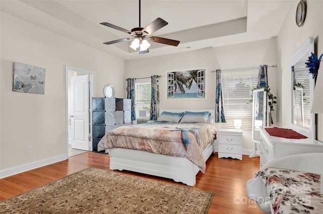 bedroom with a raised ceiling, ceiling fan, and light hardwood / wood-style floors