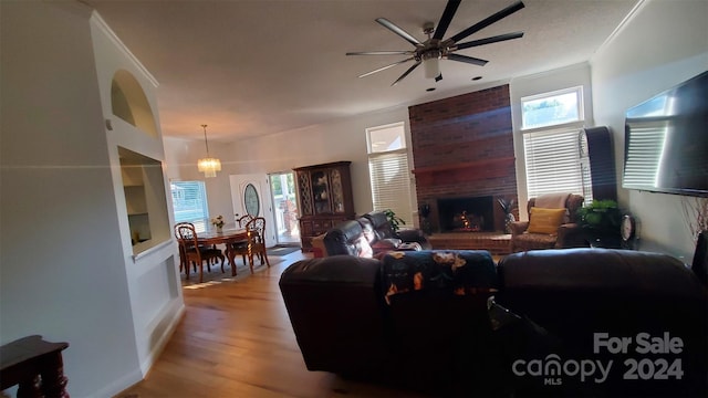 living room featuring a brick fireplace, ceiling fan with notable chandelier, ornamental molding, and light hardwood / wood-style flooring