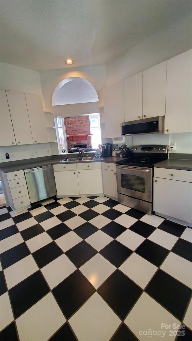 kitchen featuring a sink, dark countertops, white cabinets, appliances with stainless steel finishes, and light floors