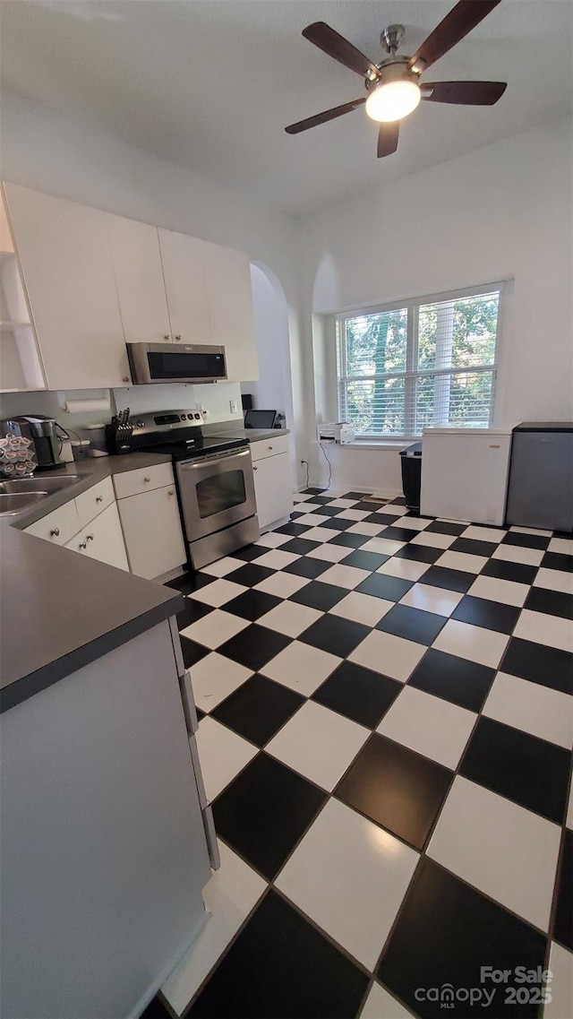kitchen with white cabinetry, a sink, dark countertops, appliances with stainless steel finishes, and light floors