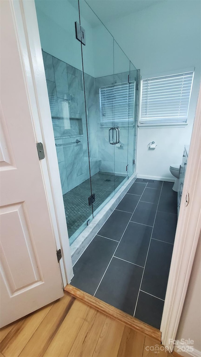 full bathroom with a stall shower, baseboards, wood finished floors, and toilet