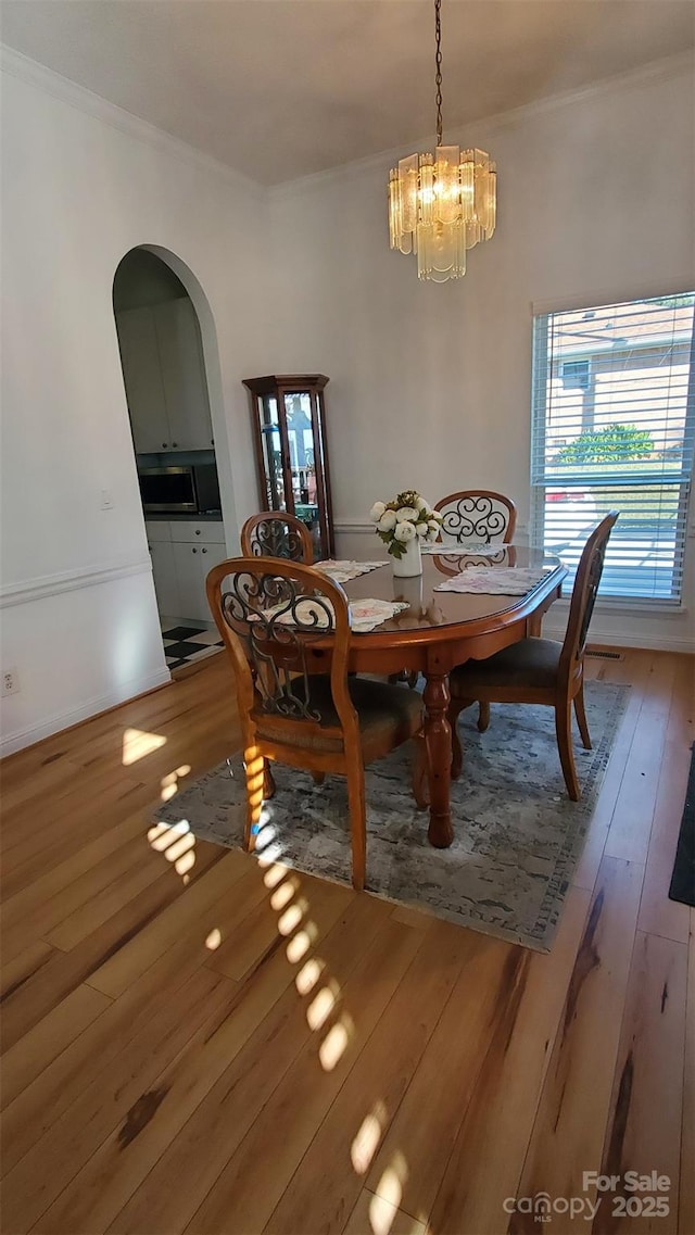 dining room with arched walkways, ornamental molding, an inviting chandelier, and hardwood / wood-style flooring