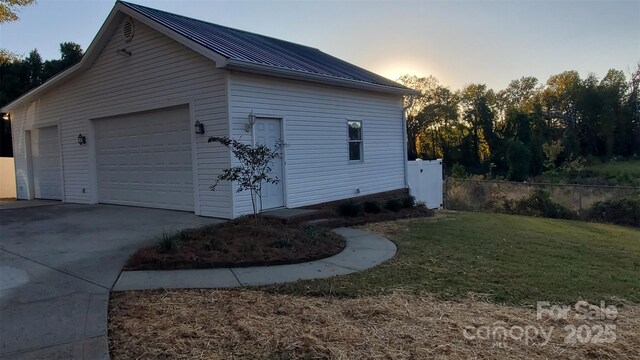 view of property exterior featuring a lawn, metal roof, a garage, and fence