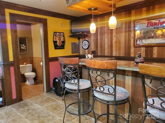 bar featuring a wainscoted wall, tile patterned floors, wood walls, indoor bar, and hanging light fixtures