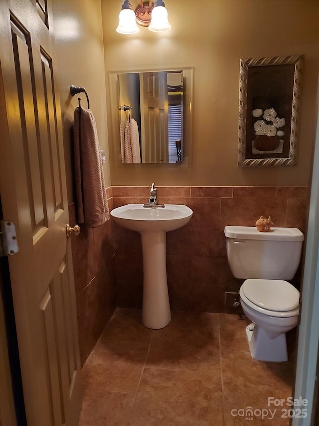 half bathroom featuring a wainscoted wall, tile patterned floors, toilet, and tile walls