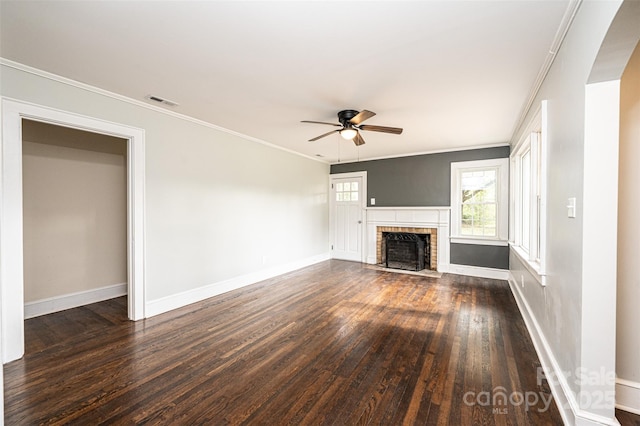 unfurnished living room featuring a brick fireplace, dark wood-type flooring, crown molding, and ceiling fan