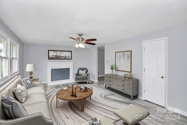 living room featuring ceiling fan, a textured ceiling, light hardwood / wood-style floors, and a brick fireplace