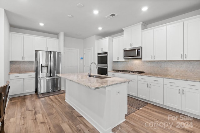 kitchen with stainless steel appliances, white cabinetry, sink, light stone countertops, and light wood-type flooring