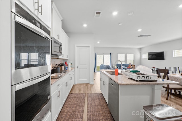 kitchen with stainless steel appliances, white cabinets, sink, a kitchen island with sink, and light wood-type flooring