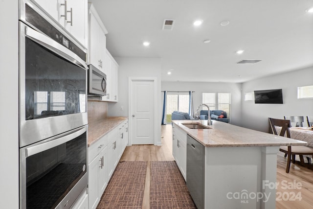 kitchen with stainless steel appliances, sink, an island with sink, light hardwood / wood-style flooring, and white cabinets