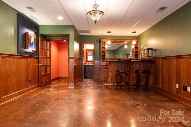 bar with a drop ceiling, decorative light fixtures, and wooden walls