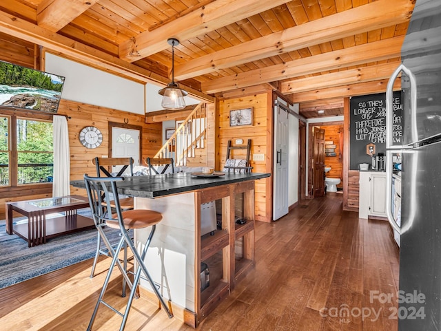 kitchen with beam ceiling, dark wood-type flooring, decorative light fixtures, and wooden walls