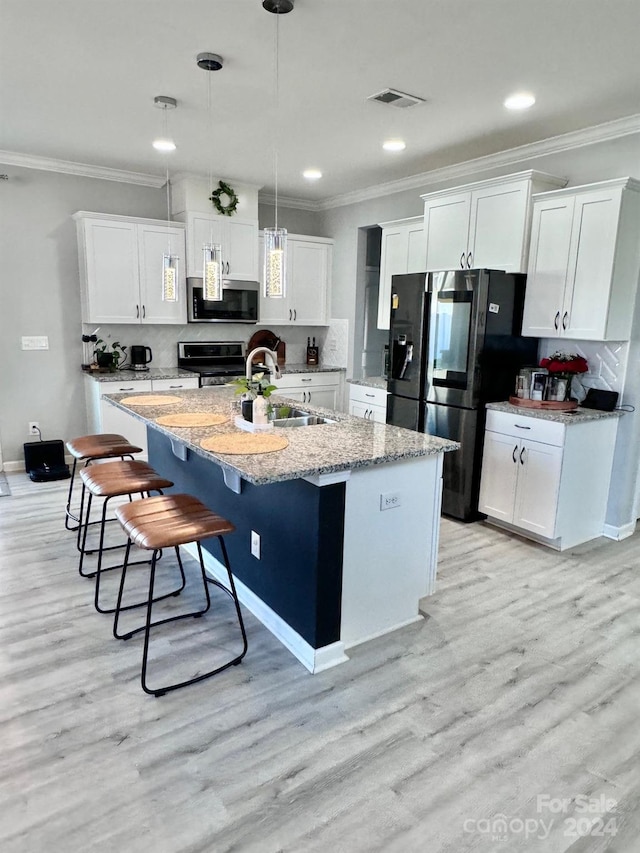 kitchen with appliances with stainless steel finishes, white cabinets, sink, and a center island with sink