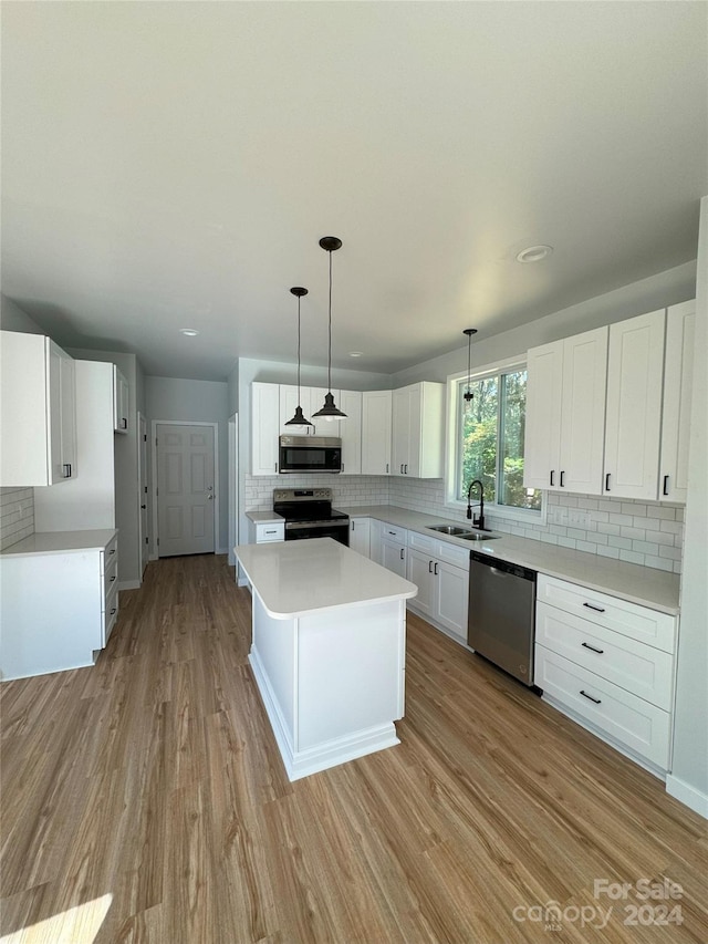 kitchen with appliances with stainless steel finishes, sink, light wood-type flooring, hanging light fixtures, and white cabinets