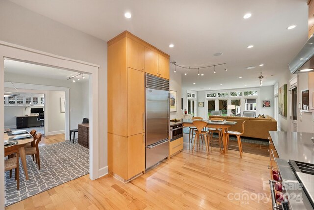 kitchen with light brown cabinets, track lighting, appliances with stainless steel finishes, and light hardwood / wood-style flooring