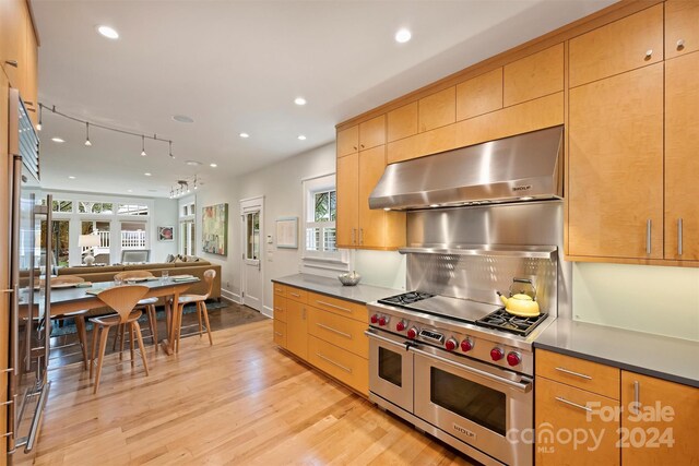 kitchen with ventilation hood, a healthy amount of sunlight, range with two ovens, and light hardwood / wood-style floors