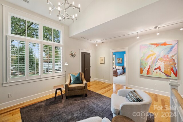 sitting room with hardwood / wood-style flooring, an inviting chandelier, and lofted ceiling