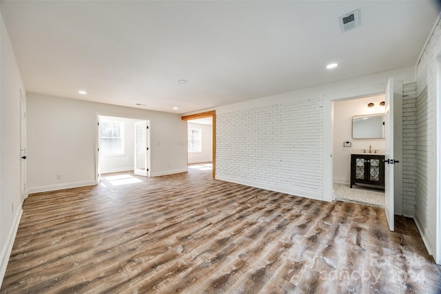 spare room featuring brick wall and light wood-type flooring