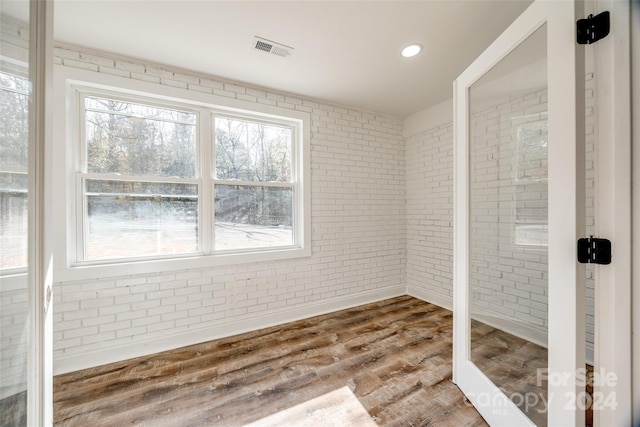 unfurnished room with hardwood / wood-style floors and brick wall