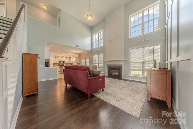 living room featuring plenty of natural light, a fireplace, dark wood-type flooring, and a high ceiling