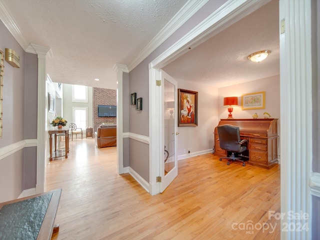 interior space featuring ornamental molding, decorative columns, a textured ceiling, and light wood-type flooring