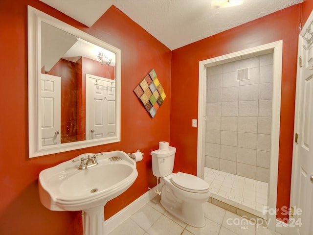 bathroom with a tile shower, a textured ceiling, toilet, sink, and tile patterned floors