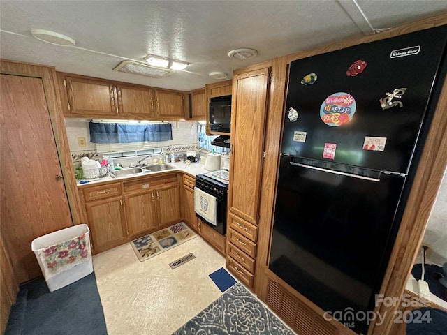 kitchen featuring backsplash, a textured ceiling, light tile patterned flooring, black appliances, and sink