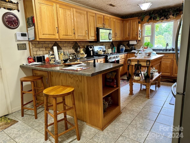 kitchen featuring light tile patterned floors, a textured ceiling, a kitchen bar, kitchen peninsula, and stainless steel appliances