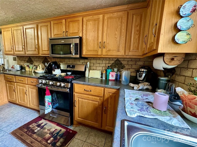 kitchen with appliances with stainless steel finishes, a textured ceiling, light tile patterned floors, and backsplash