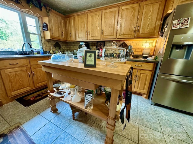 kitchen featuring sink, light tile patterned floors, a textured ceiling, tasteful backsplash, and stainless steel fridge with ice dispenser