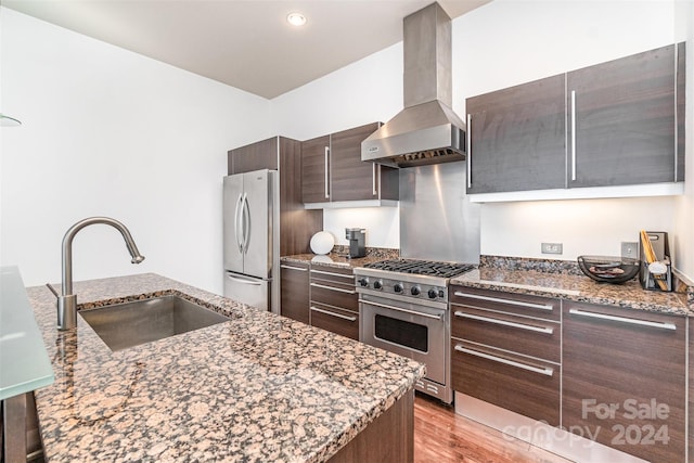 kitchen featuring wall chimney range hood, sink, appliances with stainless steel finishes, and stone countertops