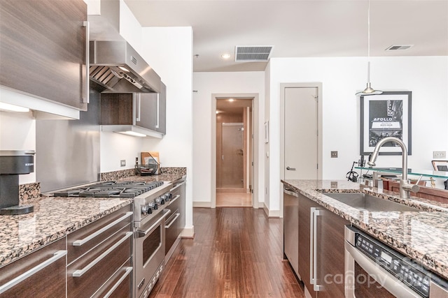 kitchen with wall chimney range hood, dark hardwood / wood-style floors, stainless steel appliances, sink, and light stone counters