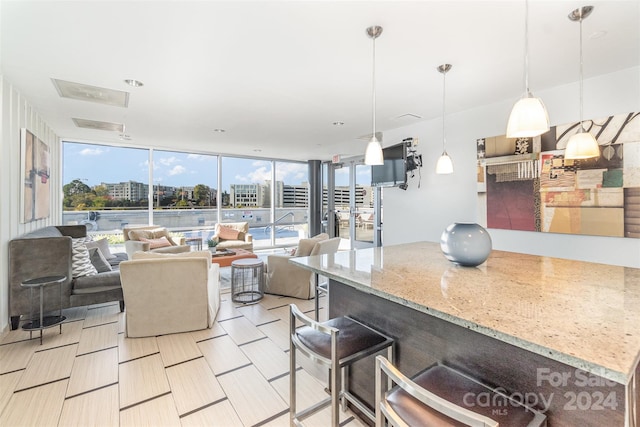 kitchen featuring expansive windows, light stone countertops, decorative light fixtures, and a breakfast bar area