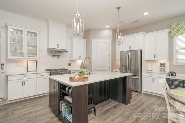 kitchen with stainless steel appliances, hardwood / wood-style flooring, white cabinetry, hanging light fixtures, and an island with sink