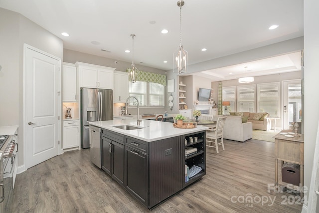 kitchen featuring white cabinets, sink, an island with sink, pendant lighting, and light hardwood / wood-style flooring