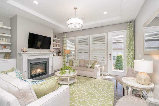 living room featuring built in shelves, wood-type flooring, a raised ceiling, and a fireplace