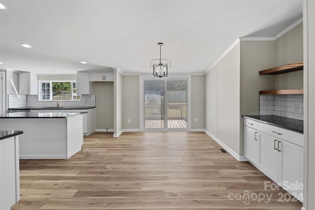 kitchen with white cabinets, backsplash, light hardwood / wood-style flooring, sink, and decorative light fixtures