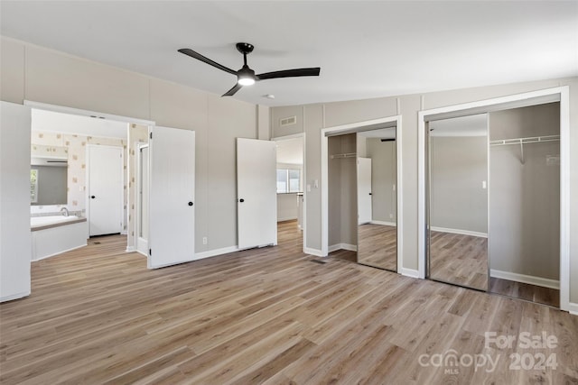 unfurnished bedroom with ensuite bathroom, light wood-type flooring, multiple closets, ceiling fan, and vaulted ceiling