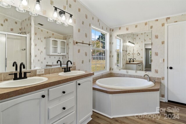 bathroom with vanity, independent shower and bath, vaulted ceiling, and hardwood / wood-style floors