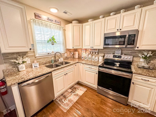 kitchen with sink, stainless steel appliances, dark wood-type flooring, light stone counters, and decorative backsplash