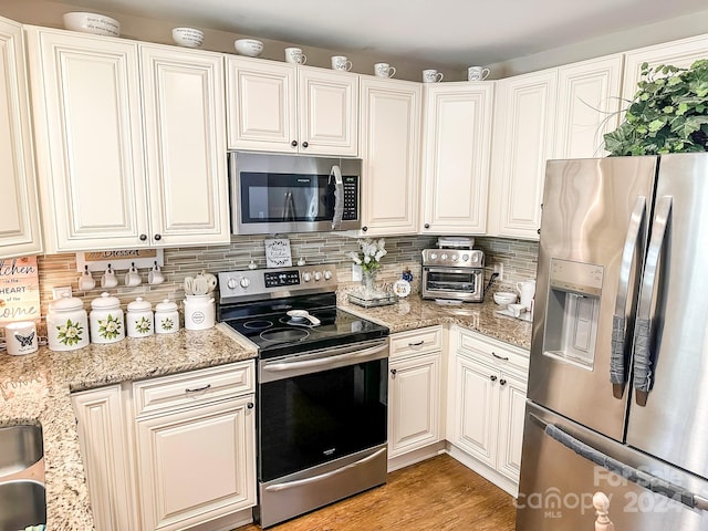 kitchen featuring stainless steel appliances, white cabinets, light stone counters, decorative backsplash, and light hardwood / wood-style flooring