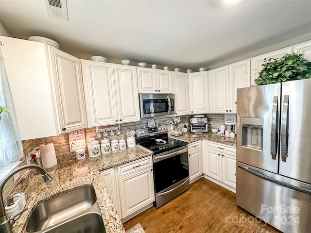 kitchen with sink, light stone countertops, white cabinets, appliances with stainless steel finishes, and tasteful backsplash