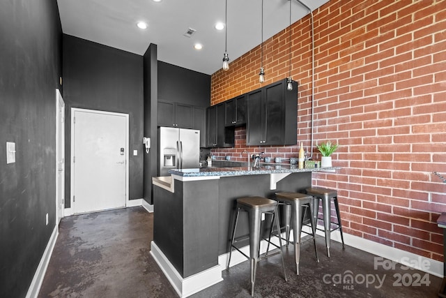 kitchen with kitchen peninsula, hanging light fixtures, a breakfast bar, stainless steel refrigerator with ice dispenser, and light stone counters